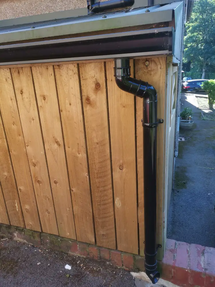 Black downpipe installed on a wooden outbuilding