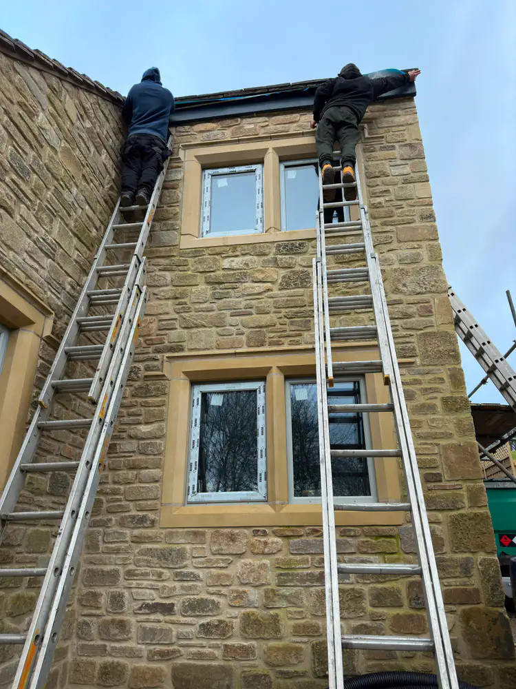 Two Gutterworx installers carrying out roofline work on a stone house